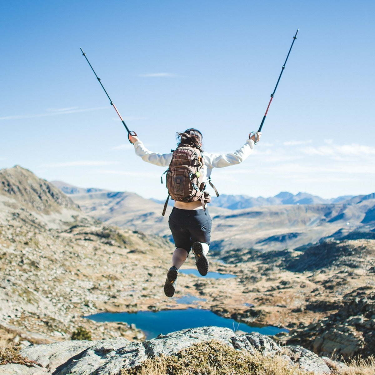 Person with a backpack jumping in the air with mountains and a lake in the background