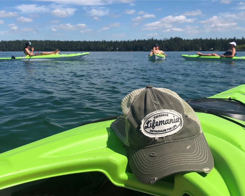 Green kayak with a cap featuring 'Lifemania' on a lake with people kayaking in the background.