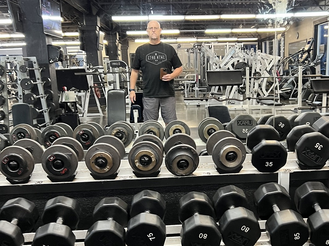 Man standing in a gym with dumbbells on the floor
